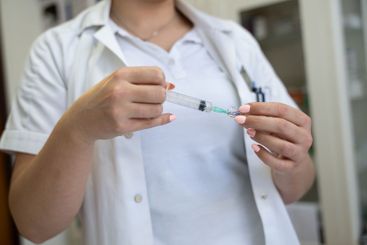 A focused nurse in a white lab coat carefully prepares a...