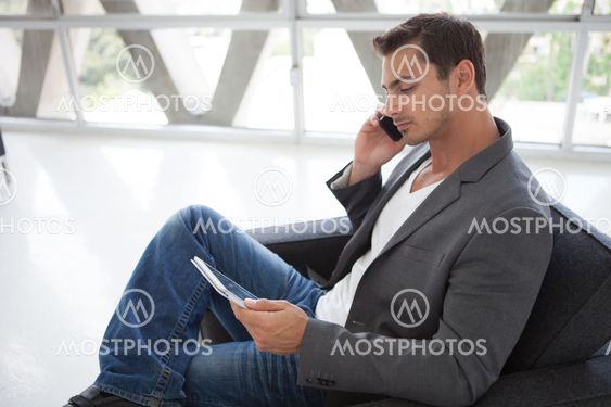 Good looking man in his 20s on his cell working on a mini think pad