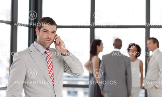 Self-assured businessman holding a phone at workplace with his colleagues
