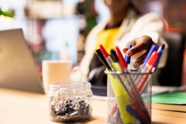 Close up of student in home office reaching for pen from...