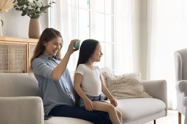 Loving young mom brushing little daughter on couch at home