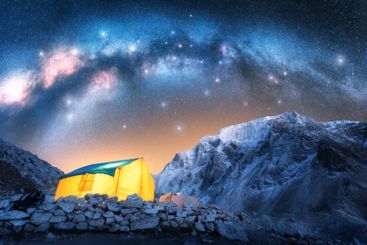 Milky Way, glowing yellow tent in snowy mountains at...