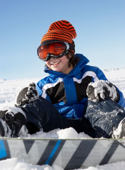Young Boy Sitting In Snow With Snowboard