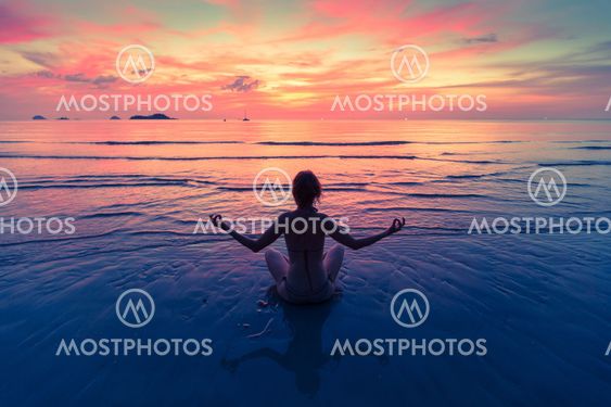 Young woman practicing yoga sitting on the sea beach during an amazing sunset.