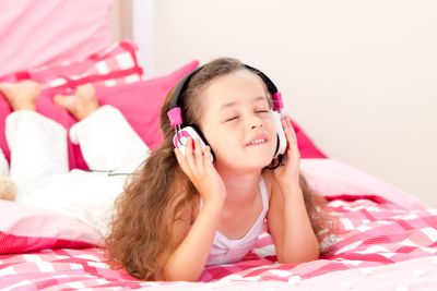 Beautiful little girl listening music lying on her bed 