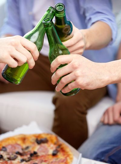 close up of friends clinking beer bottles at home