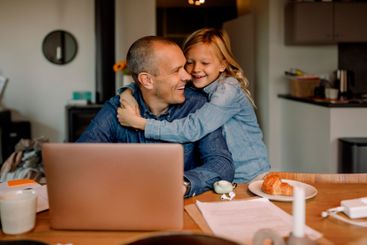 Happy boy embracing father working on laptop at home