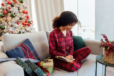 Young African woman sits on couch and writes New Year...