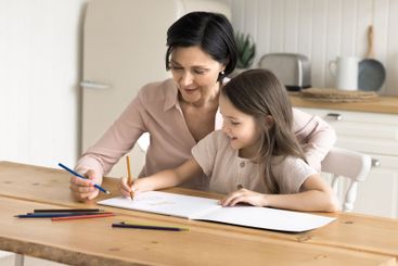 Smiling mature grandma help little granddaughter draw...