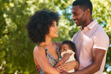 Loving Parents Cuddling Sleeping Baby Daughter Outdoors...