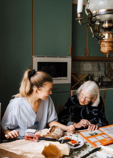 Smiling nurse teaching senior woman at dinning table in...