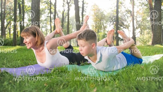 Photo of teenage boy doing yoga with his mother on grass...