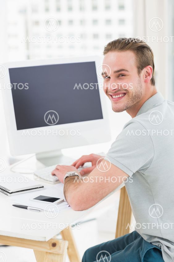 Smiling businessman sitting at desk typing on keyboard