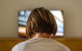 Rear view of female person sitting on sofa and watching...
