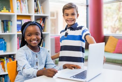 Portrait of smiling school kids using a laptop in library