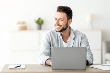 Happy freelance man working on laptop in home office,...