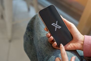 A close-up of a woman sits indoors, using X application...