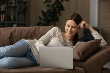 Young female lying on sofa working from home on laptop