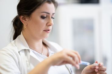 A focused nurse in a white lab coat carefully prepares a...