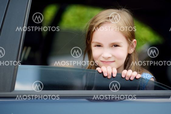 A little girl is sticking her head out the car window
