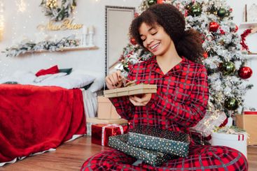 Charming young African woman sits under Christmas tree...