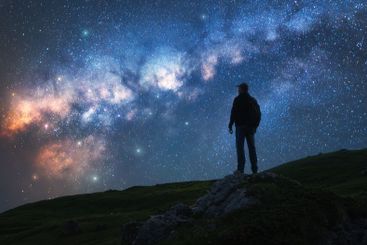 Glowing Milky Way and man on mountain peak at starry night