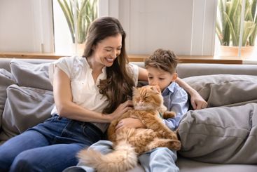 Happy mother cuddling little son boy and furry orange cat