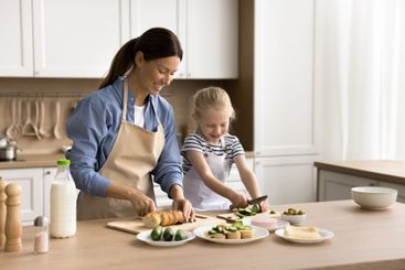 Young woman and little daughter preparing sandwiches for...