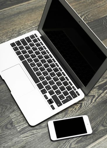 Modern laptop and smartphone placed on a dark wooden...