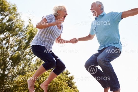 Senior Couple Bouncing On Trampoline In Garden