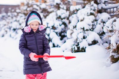 Little girl playing with red shovel in the garden