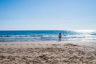 Rear view of a lonely woman standing at seashore wearing...