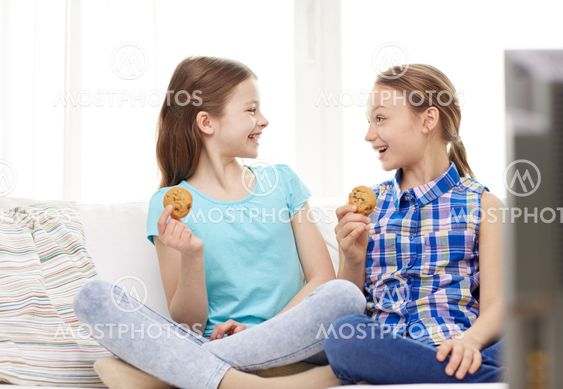 happy girls watching tv and eating cookies at home