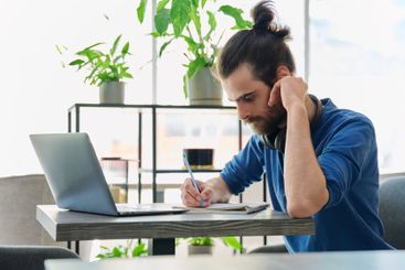 Young male university student studying using laptop,...