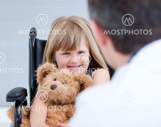Smiling little girl sitting on the wheelchair with her teddy bear