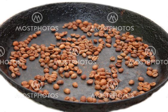 Green coffee beans roasting on the black pan