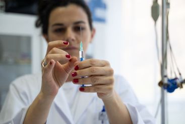 A focused nurse in a white lab coat carefully prepares a...