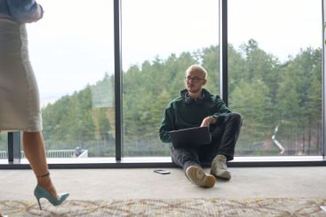 A blonde man sitting casually on the floor of a modern...