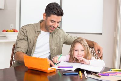 Cheerful little girl colouring at the table with her father