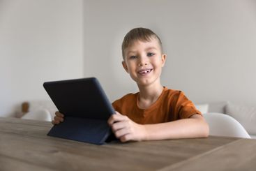 Portrait of cute little boy sitting at table with tablet