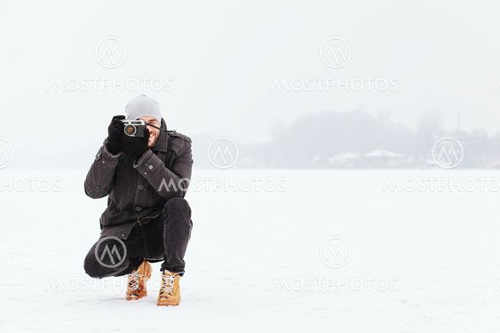 Young man taking a photo on the frozen lake in winter time
