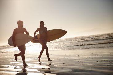 Surfing, couple and running on beach with sunset, waves...