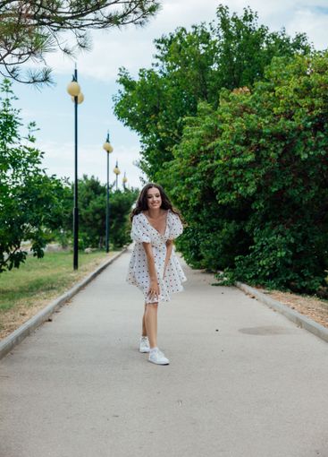 brunette woman in white polka dot summer dress walking...