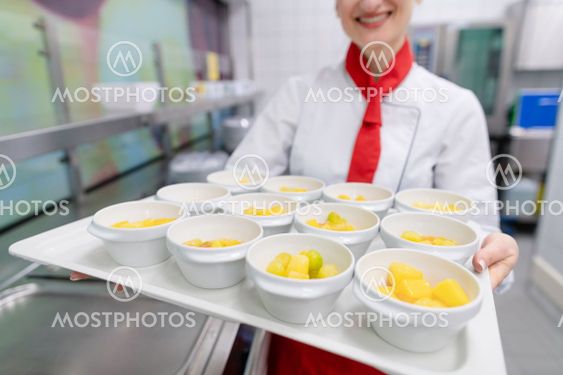 Cook in commercial kitchen showing tray with dessert