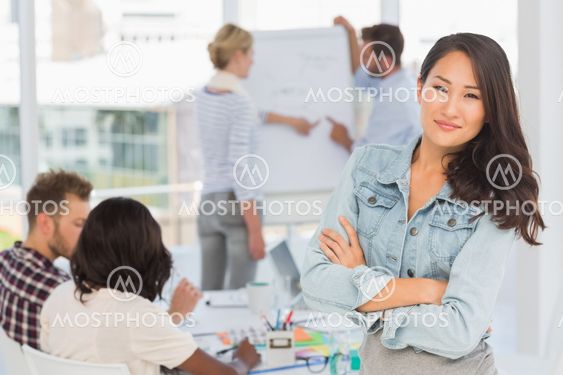 Asian woman smiling at camera while her colleagues are working