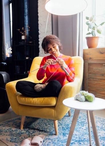 Young African smiles and knits at home in living room....
