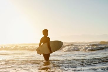 Sunset, beach and man with a surfboard in the ocean for...