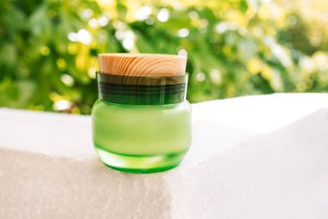 A close-up of a jar of cream made of green glass with a...