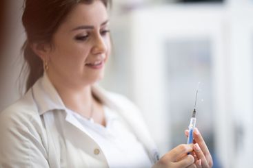 A focused nurse in a white lab coat carefully prepares a...
