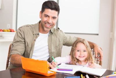 Happy little girl colouring at the table with her father